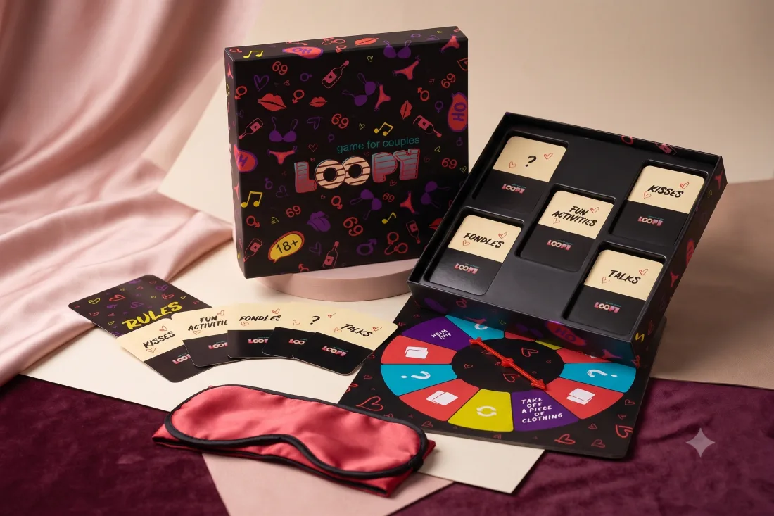 Loopy game set on pink satin: open box with five card decks, spinner board, rules card and a pink satin blindfold