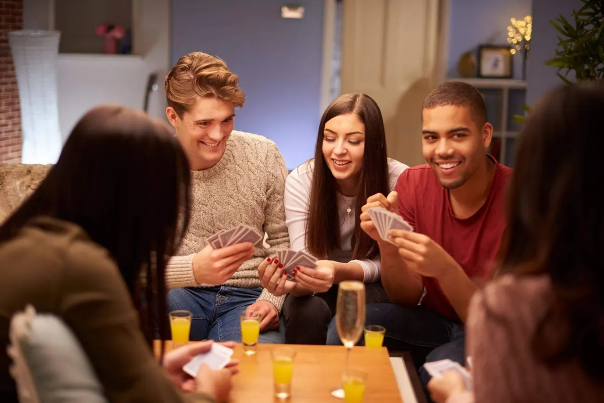 Group of friends playing cards around a low table with glasses of orange juice and champagne