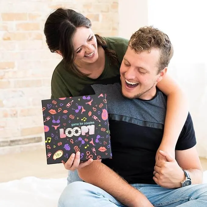 Laughing woman hugs her partner from behind while he holds up the Loopy game box